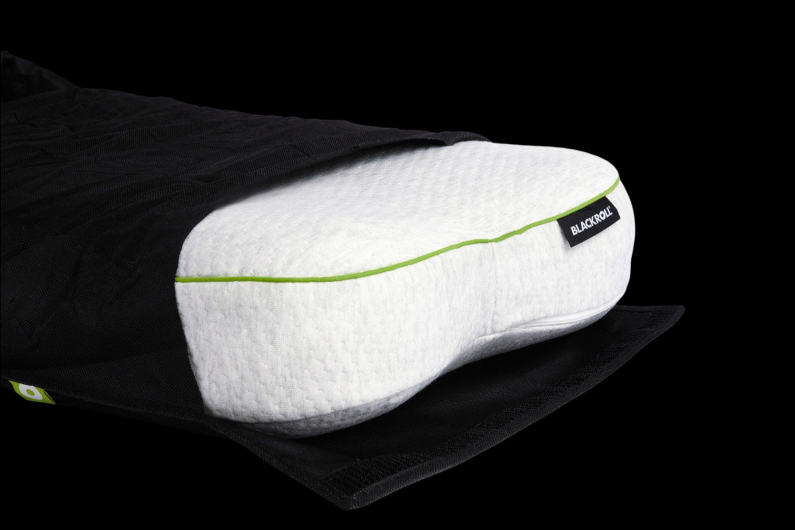 Side-profile studio frame of the Recovery Pillow Plus with lime piping, showing thickness against its travel bag on black